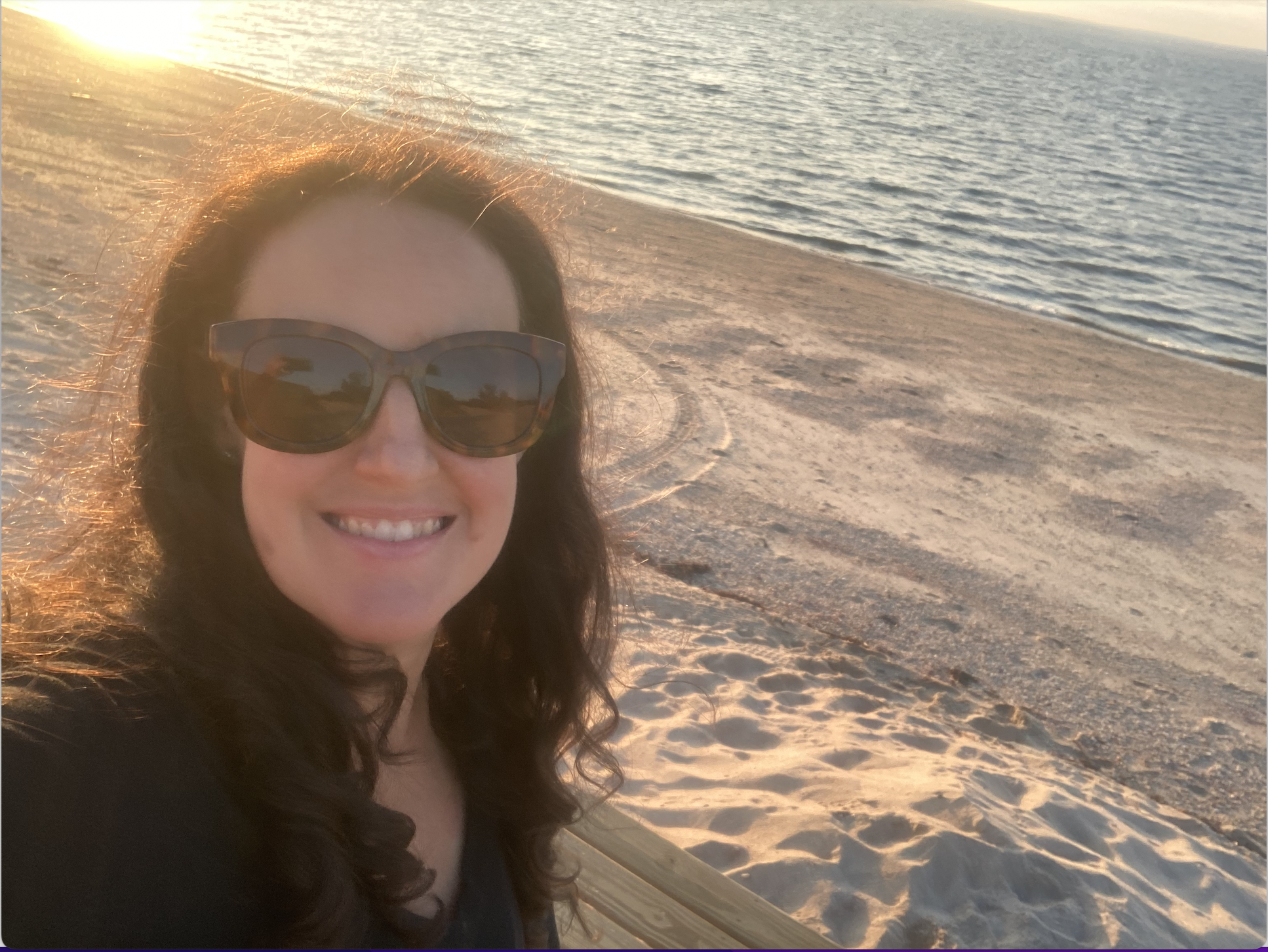 Selfie sunset of a woman with dark wavy hair and sunglassses at the beach